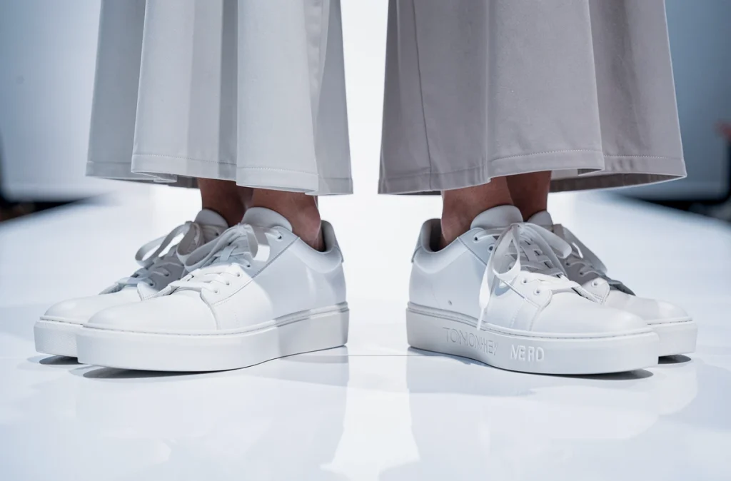 Gros plan sur deux paires de baskets blanches côte à côte sur un podium de défilé de luxe, cuir lisse et semelle plateforme